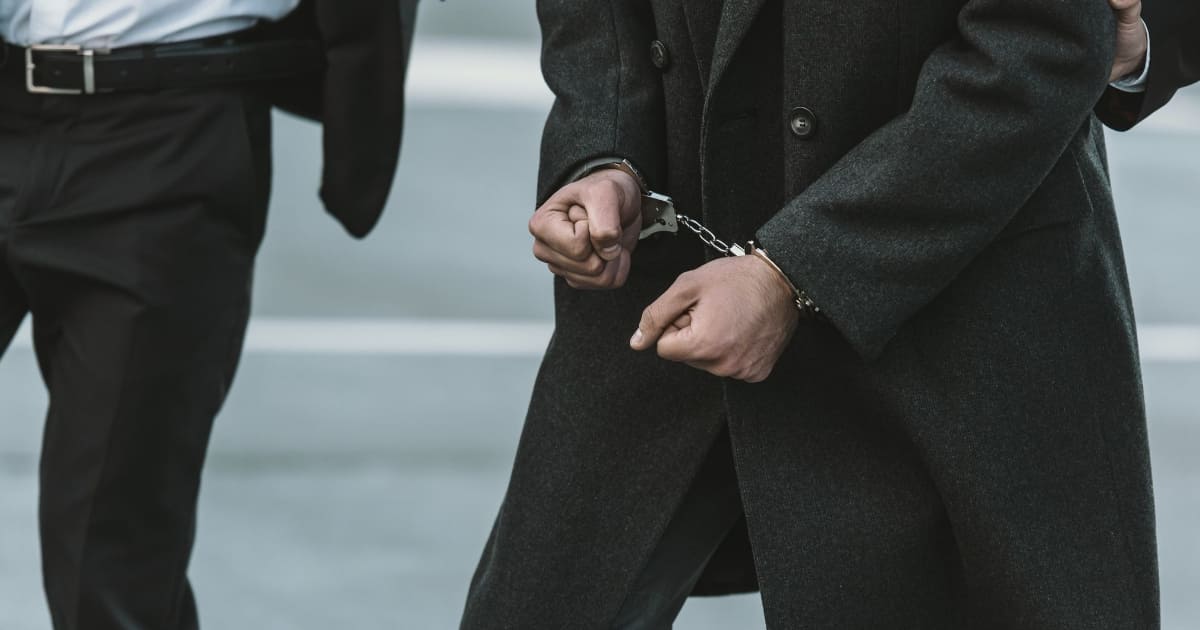 IMPACT News Organized Crime This photo depicts an individual wearing a dark suit and shackled with hand cuffs.